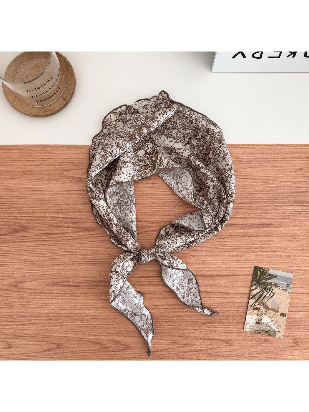 Brown floral scarf on an ivory ground tied in a loop with contrasting edges and pointed ends.