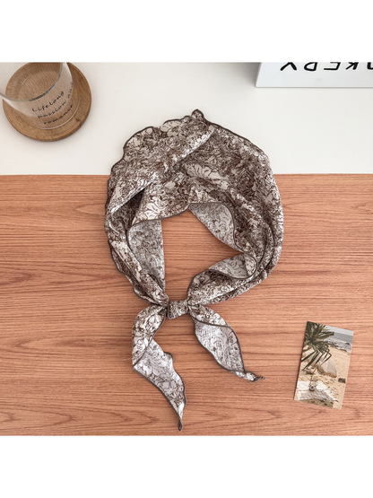 Brown floral scarf on an ivory ground tied in a loop with contrasting edges and pointed ends.