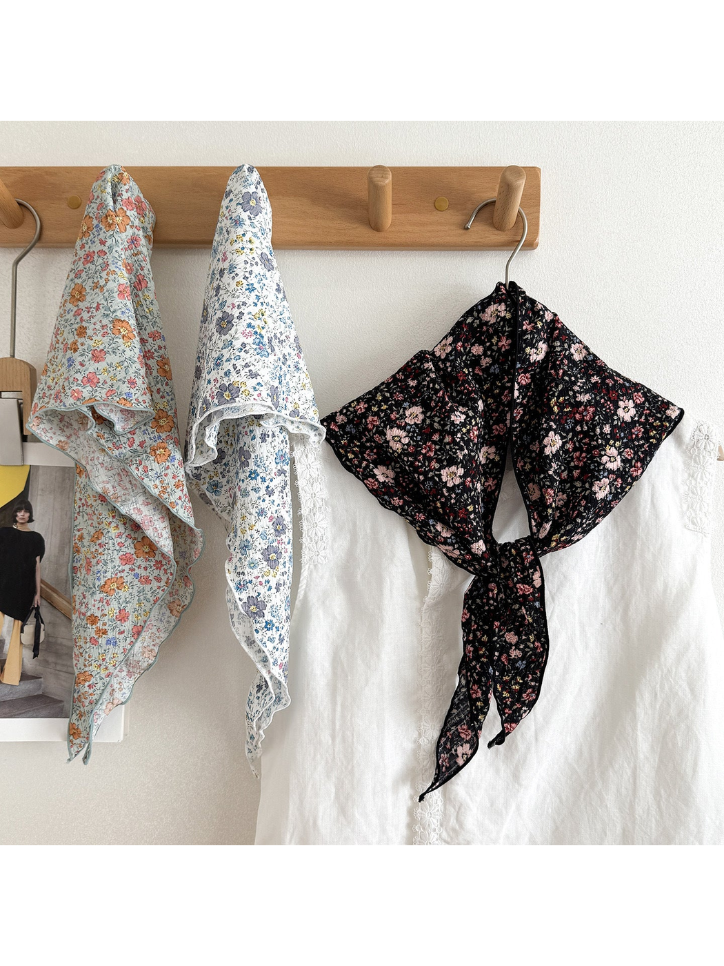 Three floral scarves hanging from wooden hooks, with the black scarf tied over a white blouse.