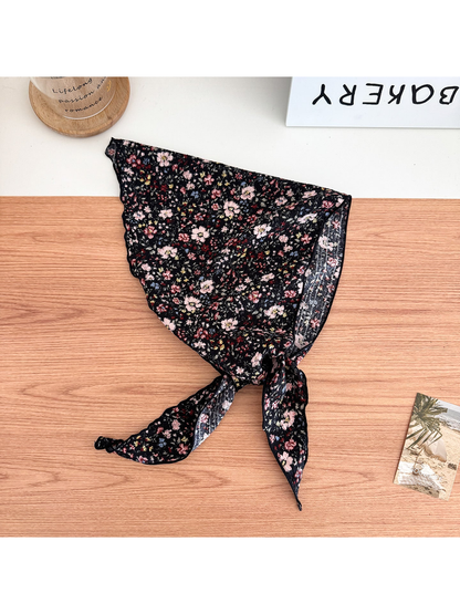 Black floral triangle scarf with tied pointed ends on a wooden surface.