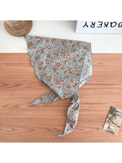 Orange floral triangle scarf with tied pointed ends on a wooden surface.