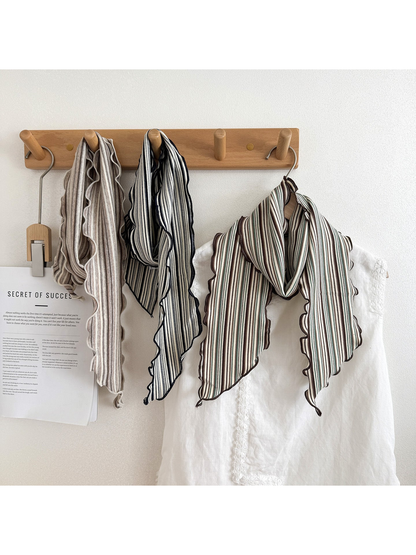 Three striped scarves with wavy edges hanging from a wooden rack, with one draped over a white top.