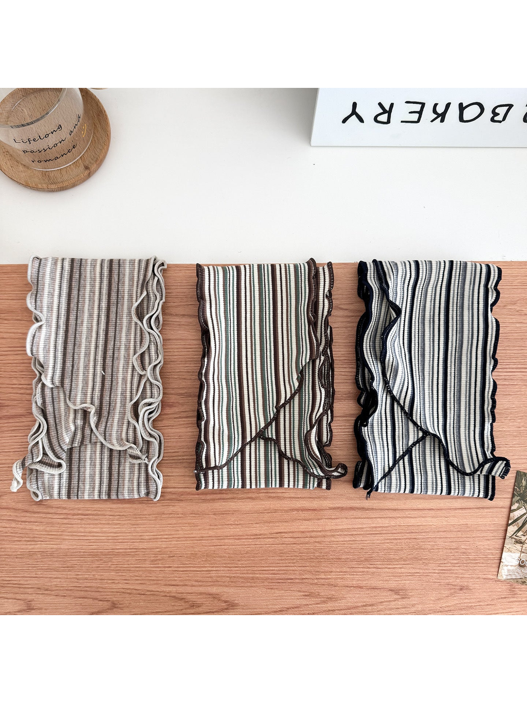 Beige, Green and Black striped scarves folded side by side, showing their wavy edges.