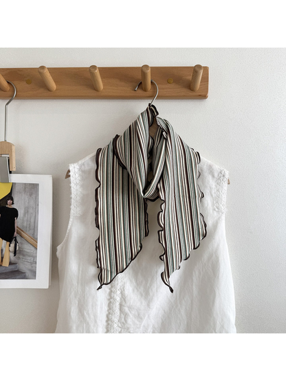 Green striped scarf draped over a white top on a hanger beside a magazine photograph.