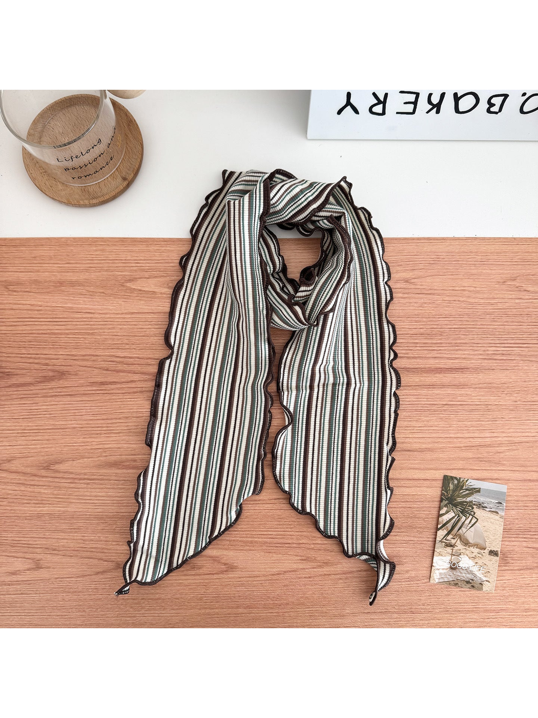 Green striped scarf arranged in a loop with wavy brown edges and pointed ends.