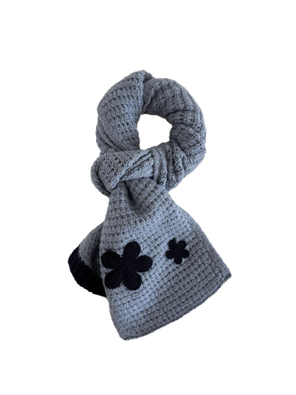 Blue textured scarf looped on a white background with contrasting flower appliqués and ribbed end trim
