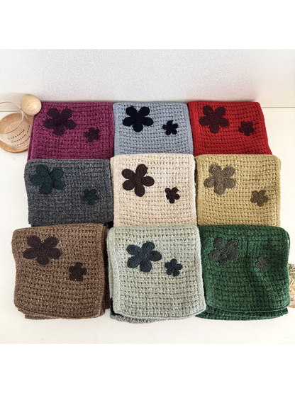 Nine scarf styles folded together, showing textured surfaces and contrasting flower appliqués