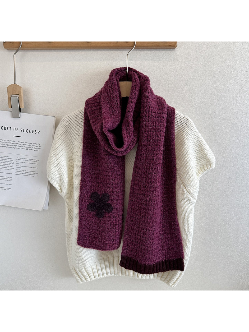 Purple textured scarf draped over a cream sweater with a contrasting flower appliqué and ribbed end trim