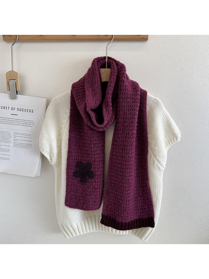 Purple textured scarf draped over a cream sweater with a contrasting flower appliqué and ribbed end trim