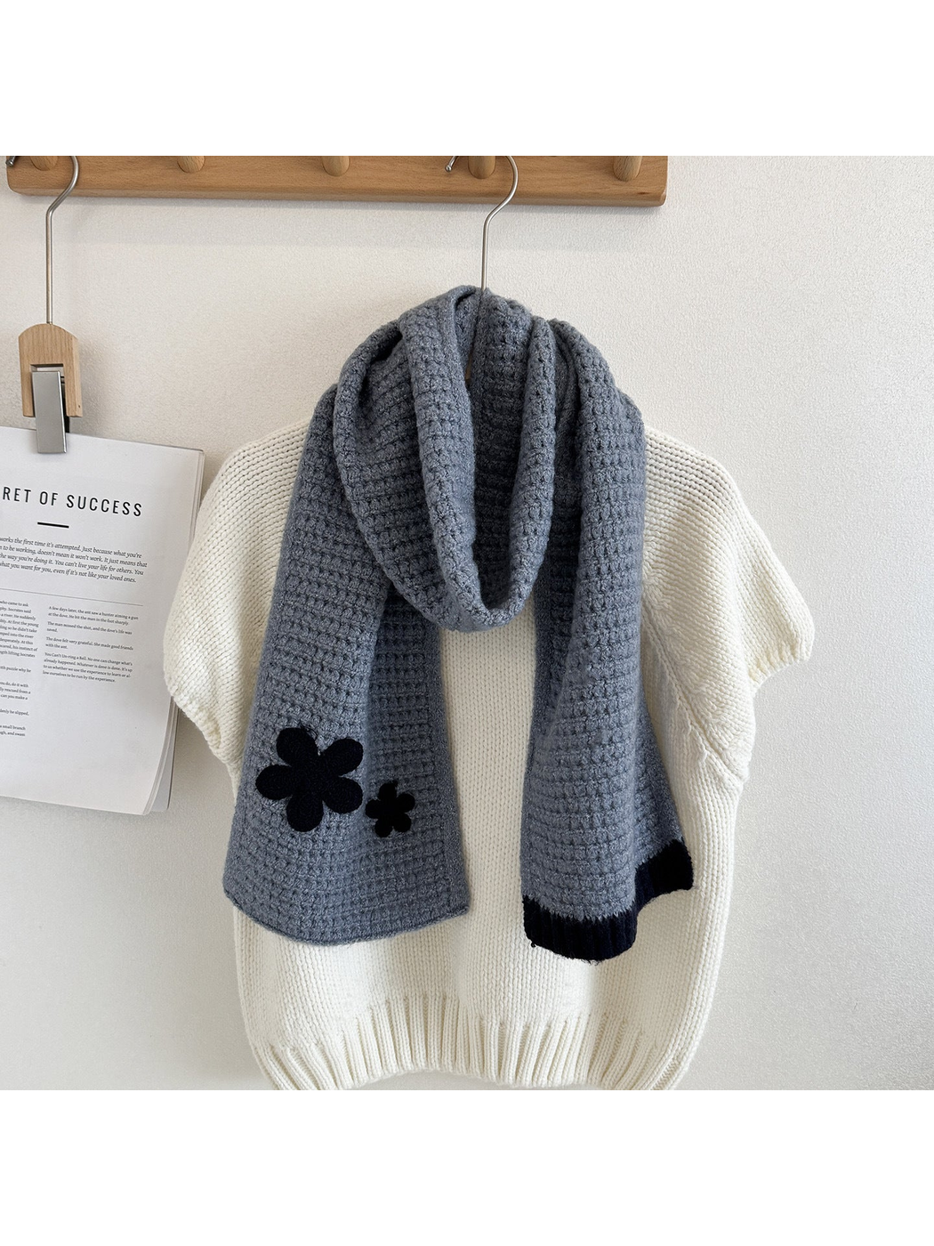 Blue scarf draped lengthwise over a cream sweater, showing two flower appliqués and contrasting end trim