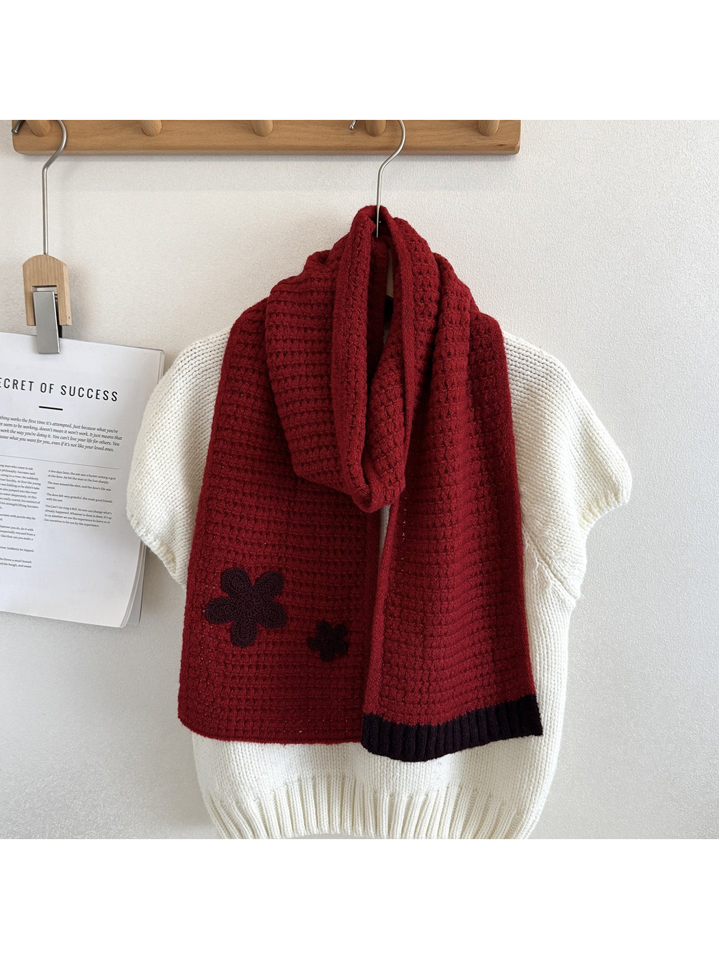 Red textured scarf draped over a cream sweater with contrasting flower appliqués and ribbed end trim