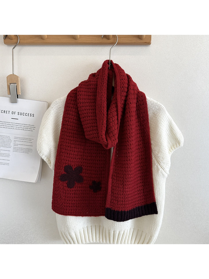 Red textured scarf draped over a cream sweater with contrasting flower appliqués and ribbed end trim