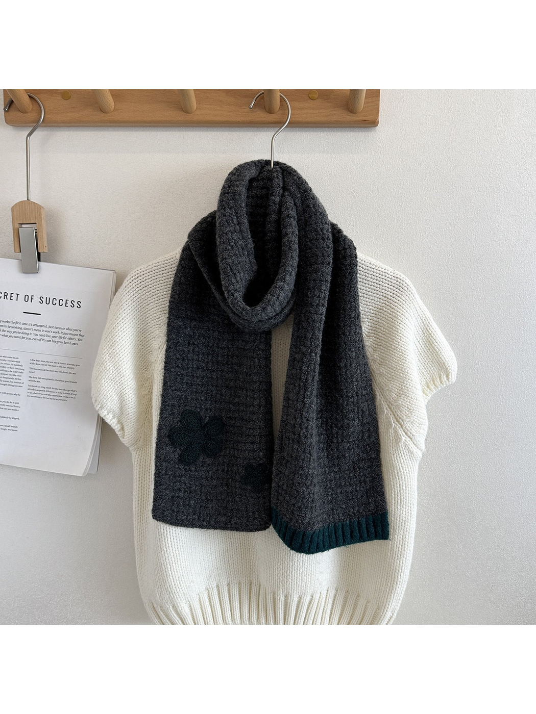 Gray textured scarf draped over a cream sweater with dark flower appliqués and contrasting ribbed end trim