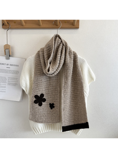 Beige textured scarf draped over a cream sweater with dark flower appliqués and contrasting ribbed end trim