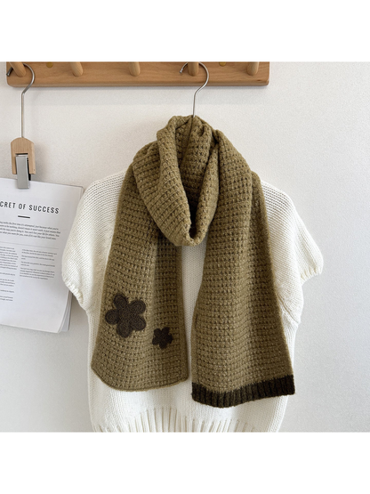 Khaki textured scarf draped over a cream sweater with contrasting flower appliqués and ribbed end trim