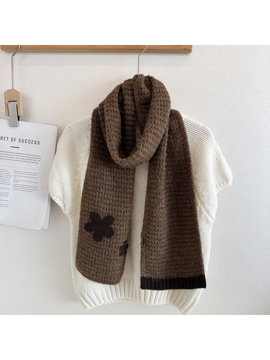 Brown textured scarf draped over a cream sweater with dark flower appliqués and contrasting ribbed end trim