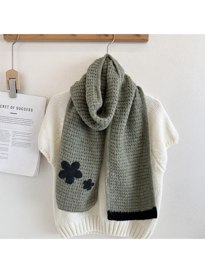 Green textured scarf draped over a cream sweater with dark flower appliqués and contrasting ribbed end trim