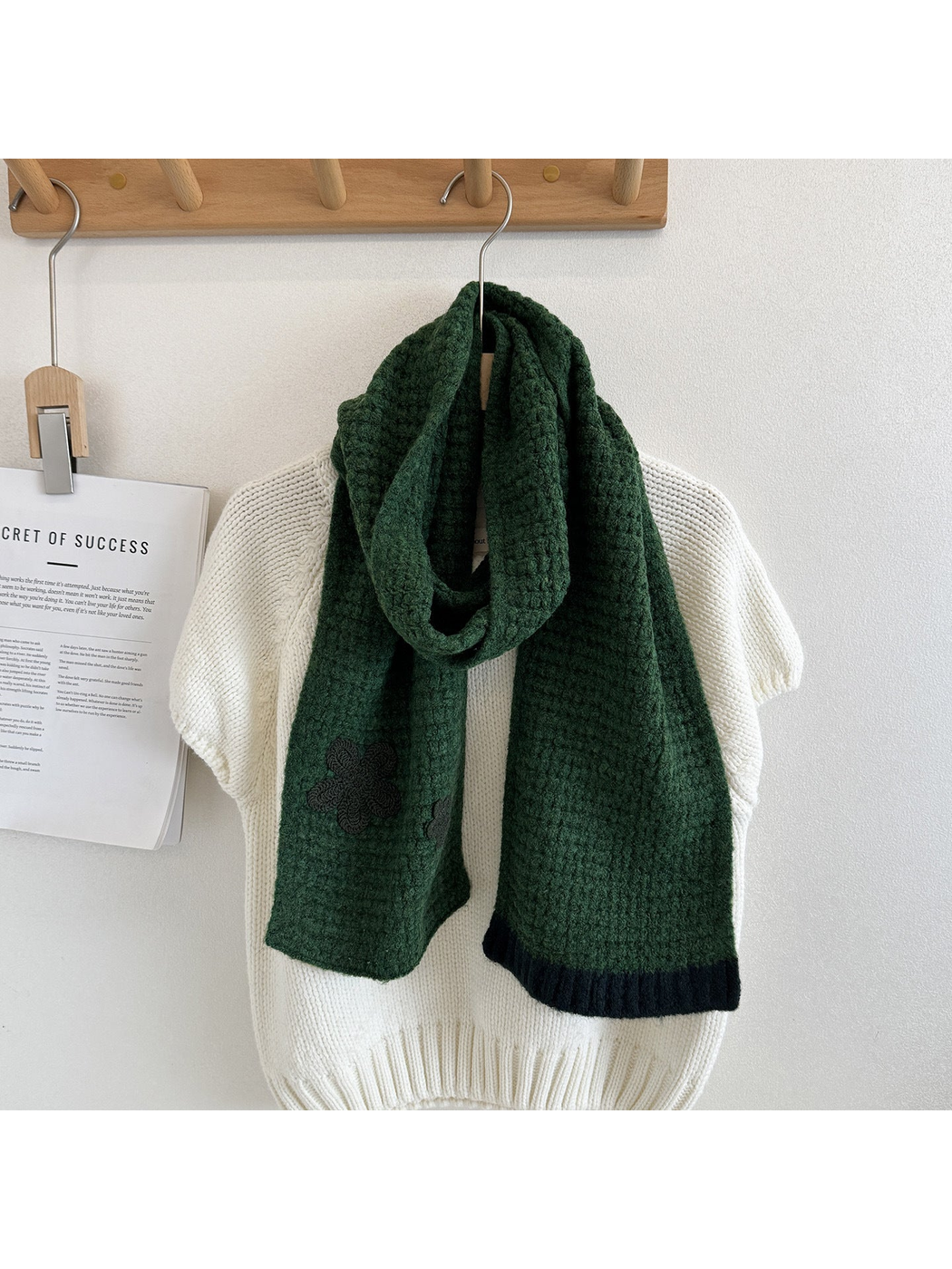 Dark Green textured scarf draped over a cream sweater with dark flower appliqués and contrasting ribbed end trim