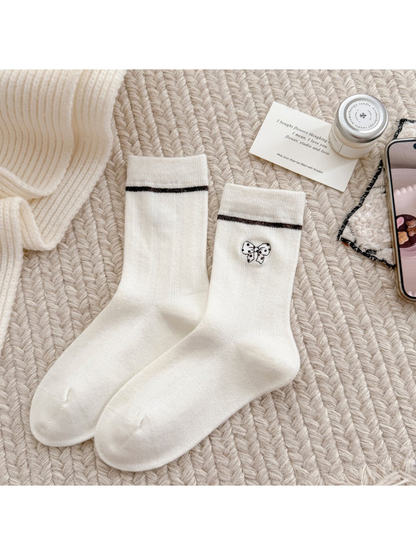Ivory socks with a spotted bow motif, dark cuff stripes and ribbed cuffs.
