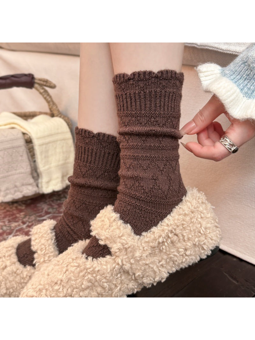 Brown patterned socks worn with fleece-textured sandals, with a hand adjusting the ankle.