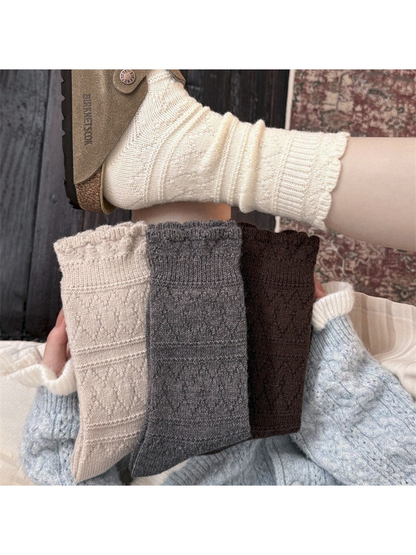 Ivory socks worn with a sandal above folded beige, gray, and brown socks held in a hand.