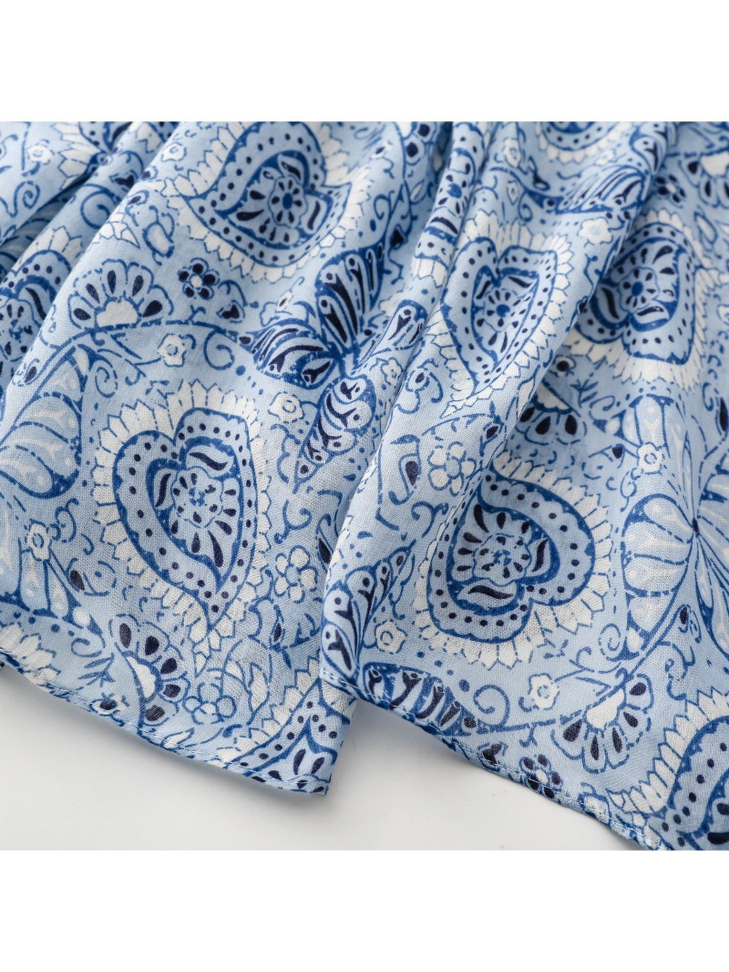 Close-up of the blue paisley, butterfly and floral print beside the narrow stitched hem