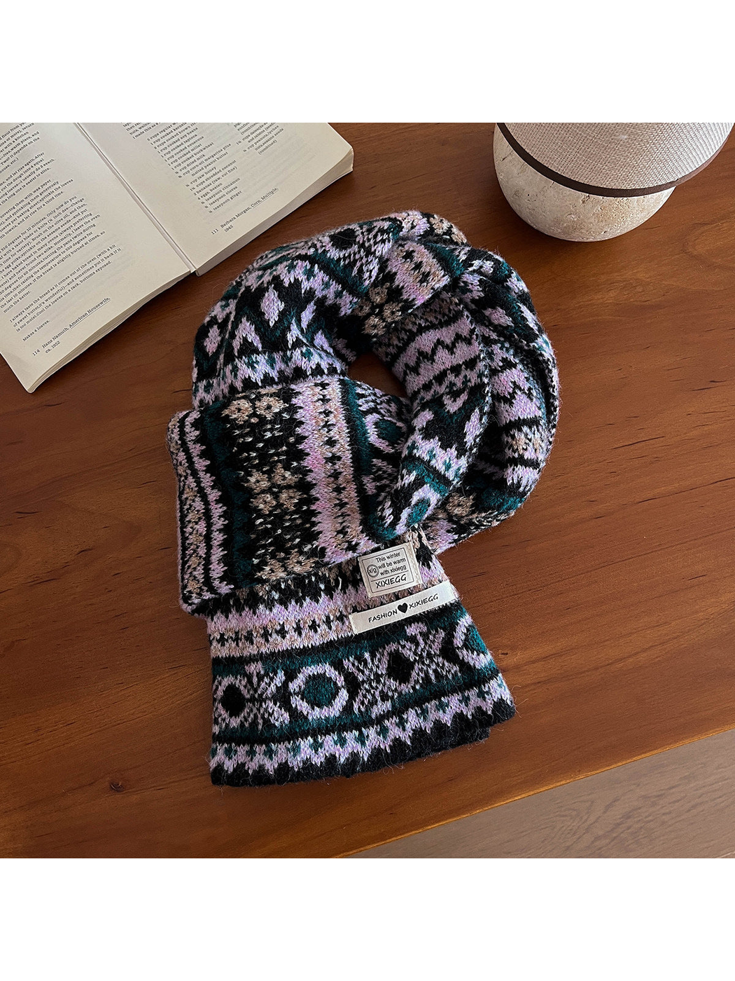 Black scarf with a lavender-pink and teal geometric pattern on a wooden table