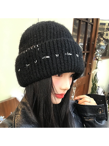 Black fuzzy ribbed beanie with contrasting stitched motifs, worn view