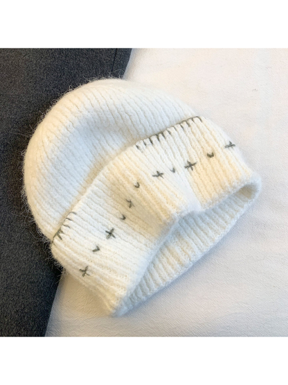White fuzzy ribbed beanie with gray stitched motifs and folded cuff
