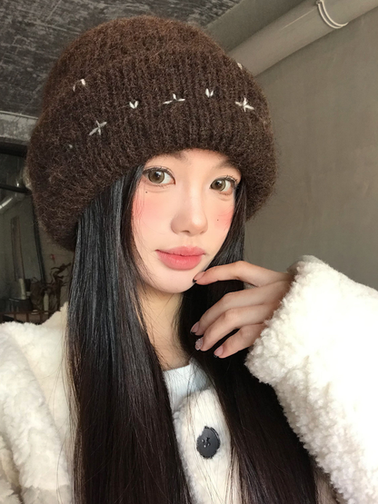 Brown fuzzy ribbed beanie with scattered stitched motifs, front worn view