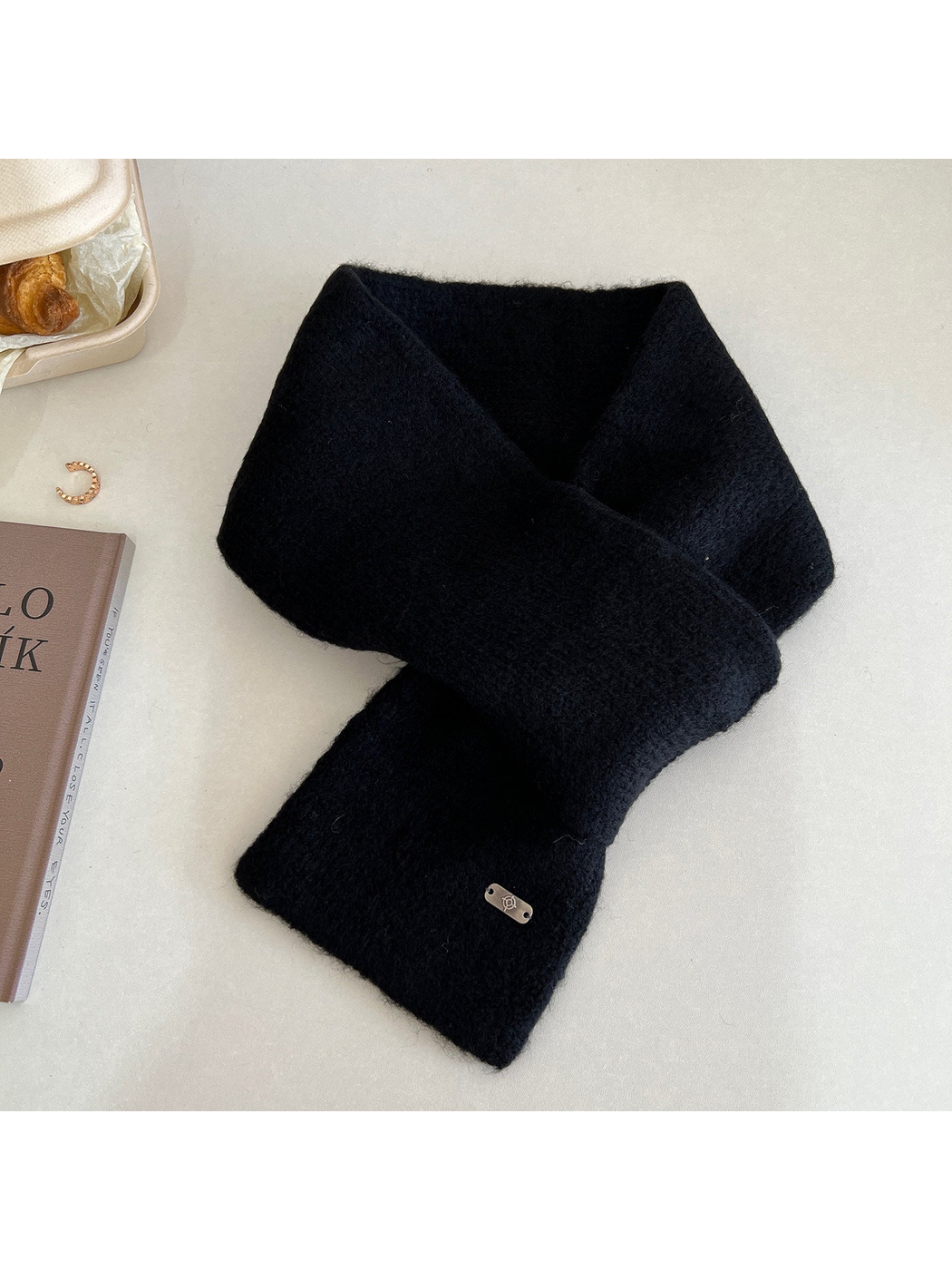 Black narrow scarf arranged in a crossed loop with a metal-tone end plaque