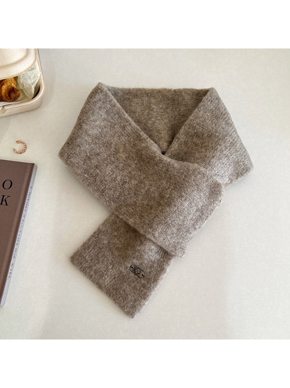 Greige narrow scarf arranged in a crossed loop with a metal-tone end plaque