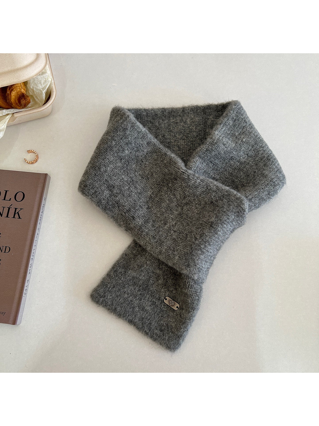 Dark gray narrow scarf arranged in a crossed loop with a metal-tone end plaque