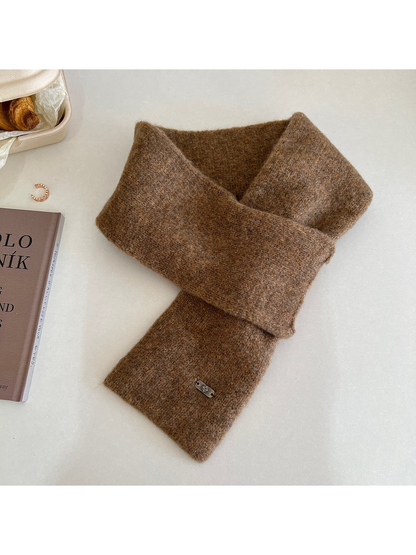 Brown narrow scarf arranged in a crossed loop with a metal-tone end plaque
