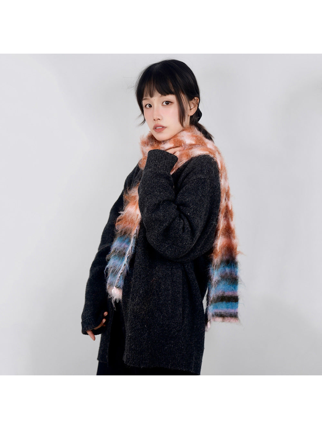 Pink, orange and blue striped fuzzy scarf worn over a dark sweater