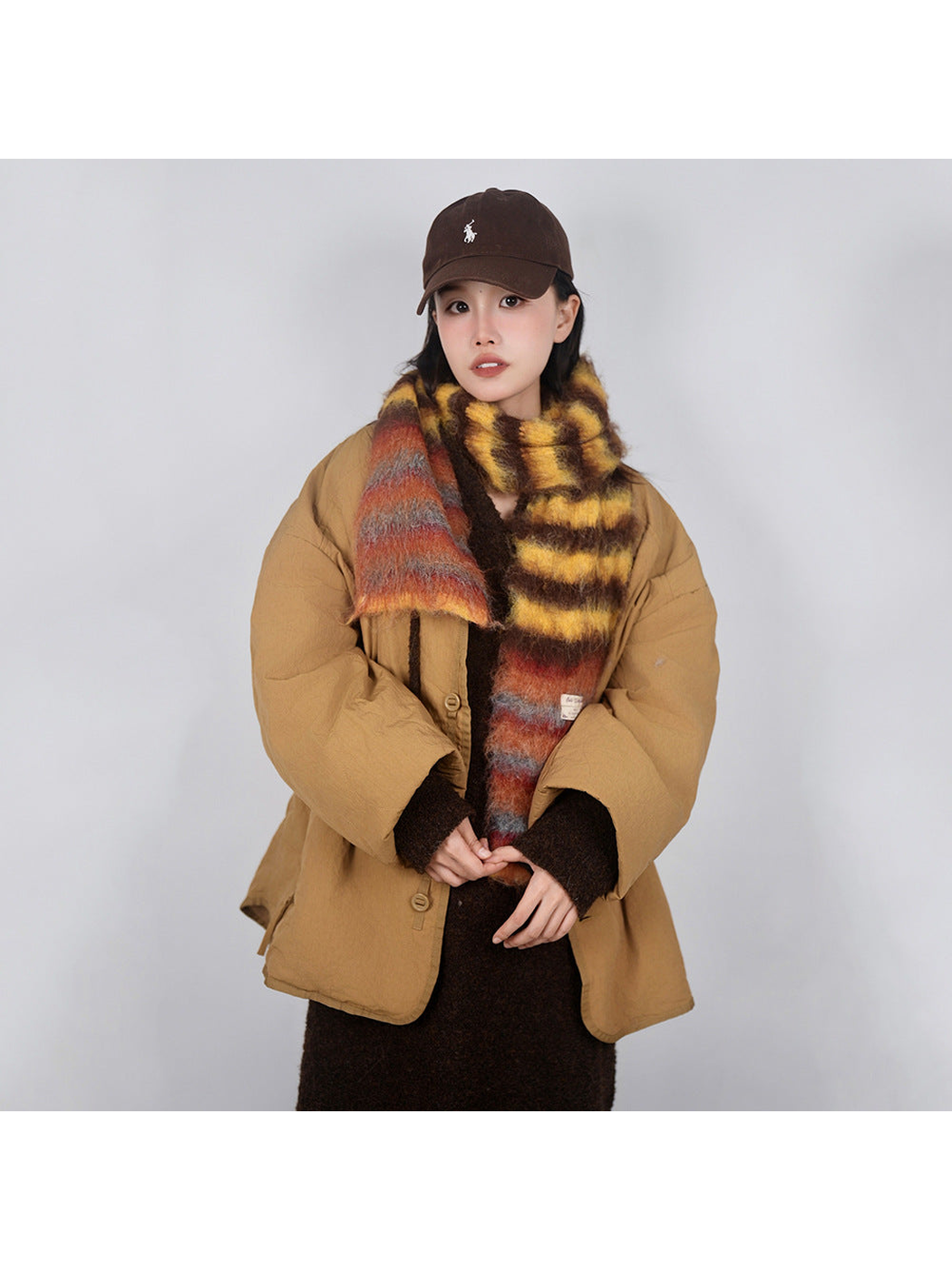 Yellow, brown and orange striped fuzzy scarf styled over a tan coat