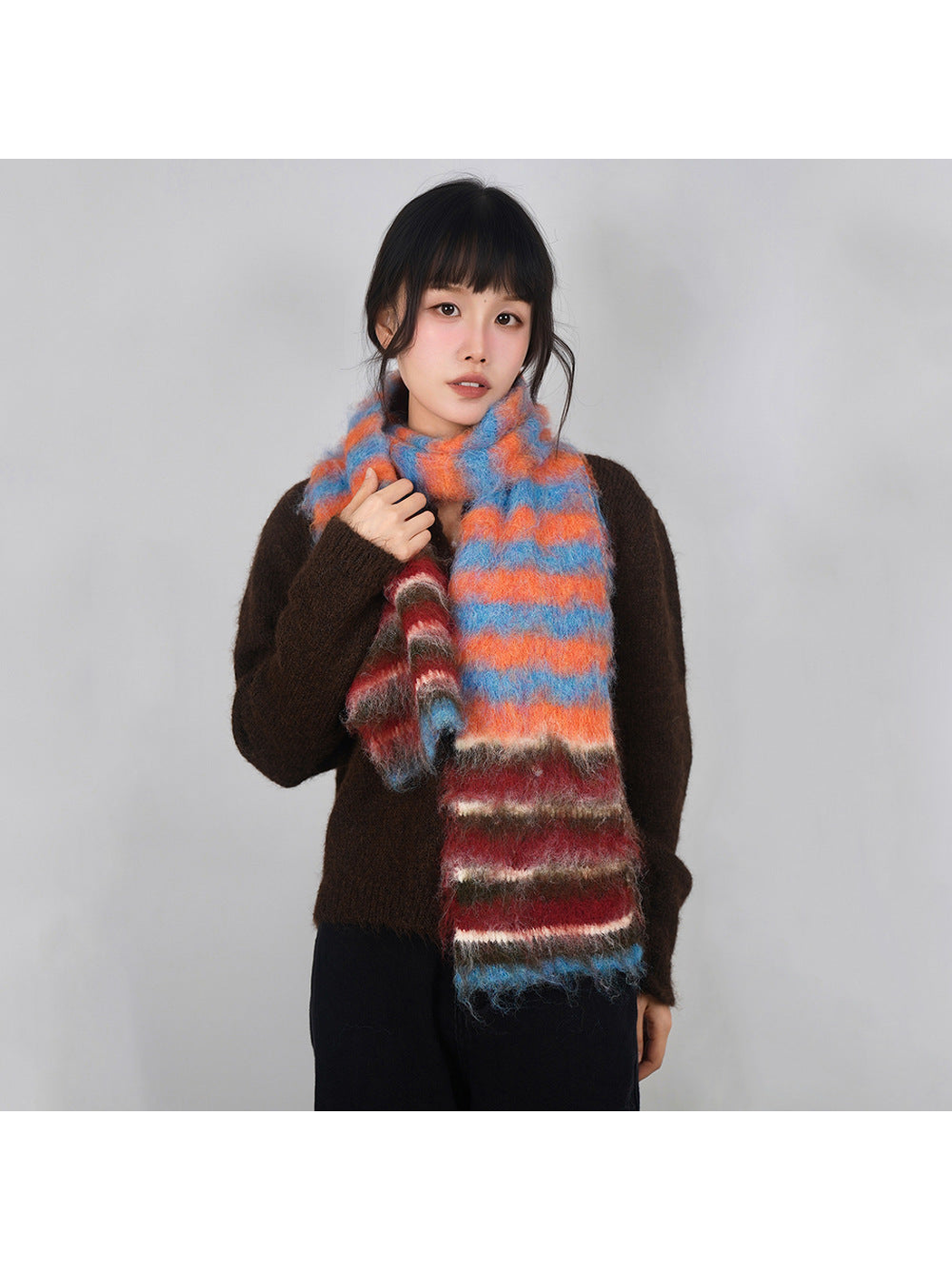 Orange, blue and red striped fuzzy scarf worn over a brown sweater
