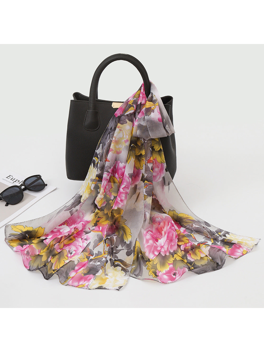 Gray, pink and yellow floral scarf draped over a black handbag