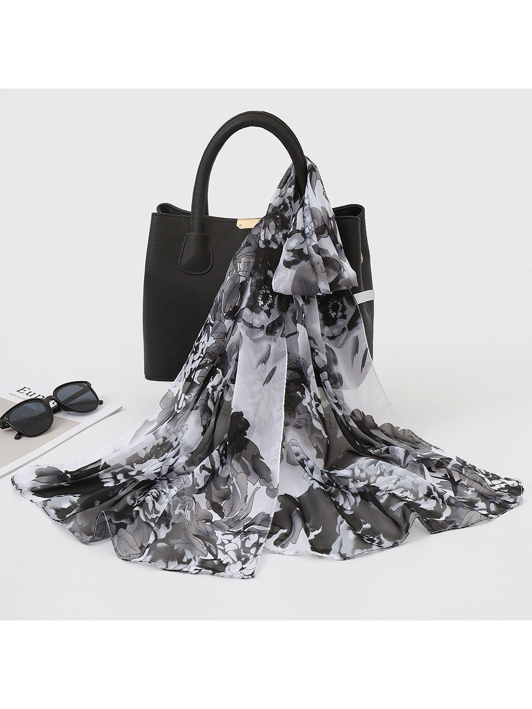 Black, white and gray floral scarf draped over a black handbag
