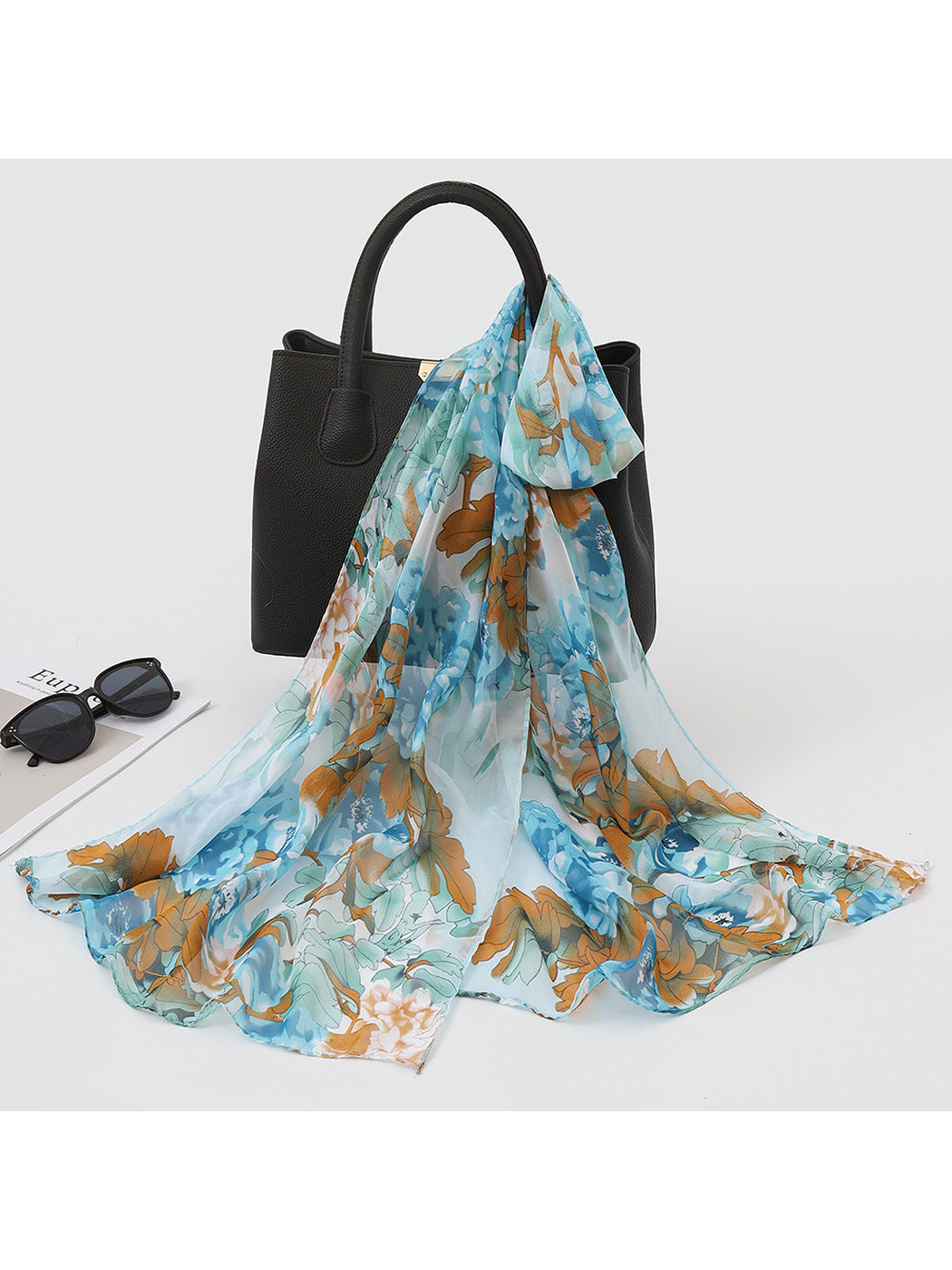 Light blue and brown floral scarf draped over a black handbag