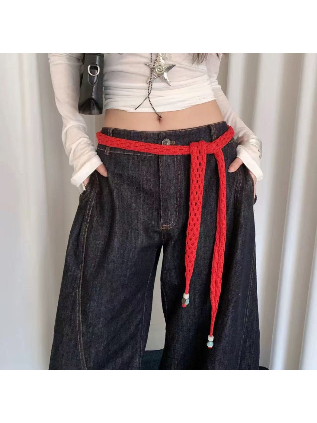 Red openwork scarf styled as a belt over dark wide-leg jeans