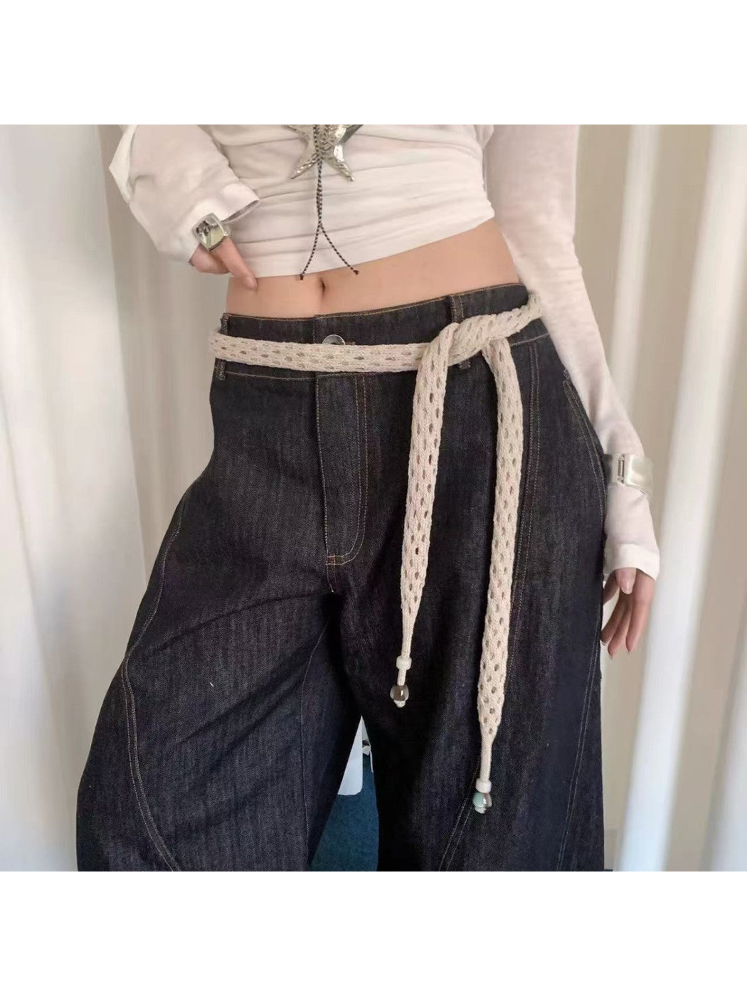 Beige openwork scarf tied at the waist over dark wide-leg jeans