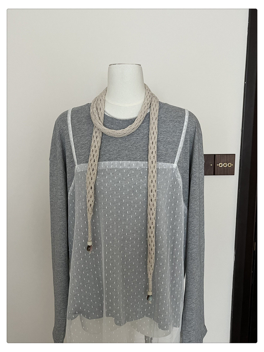 Beige openwork scarf wrapped once around a mannequin neck with long ends in front