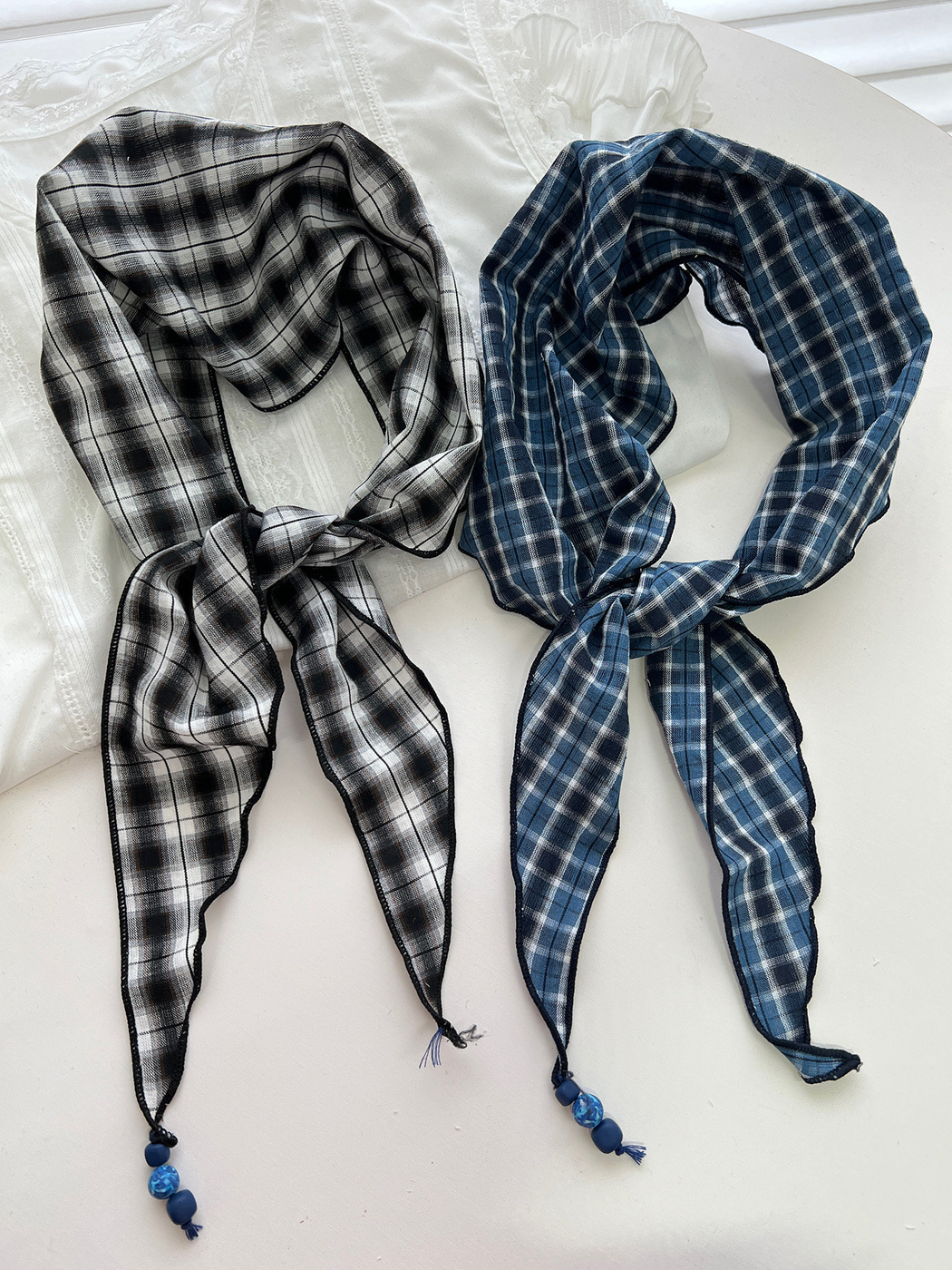 Black and gray and blue plaid triangle scarves displayed together with beaded tassels