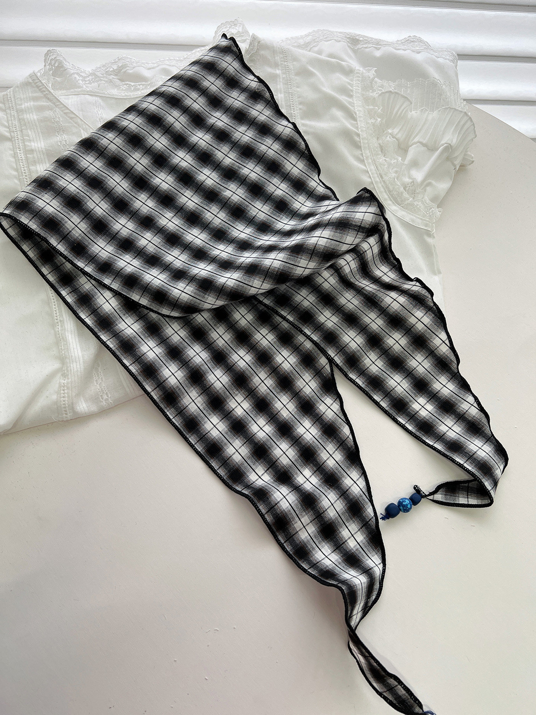 Black and gray plaid triangle scarf spread open to show its pointed shape and beaded tassel