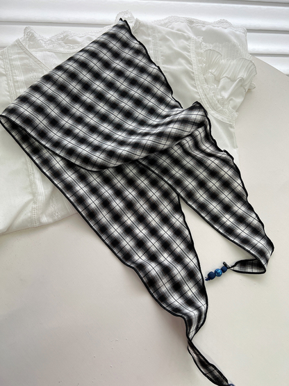 Black and gray plaid triangle scarf spread open to show its pointed shape and beaded tassel