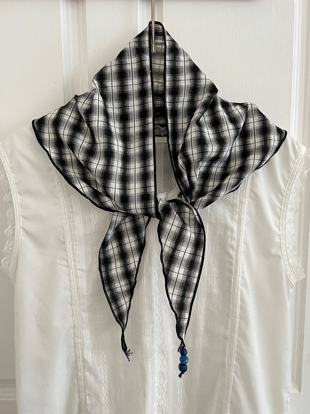 Black and gray plaid triangle scarf tied at the front over a white garment