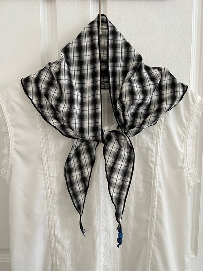 Black and gray plaid triangle scarf tied at the front over a white garment