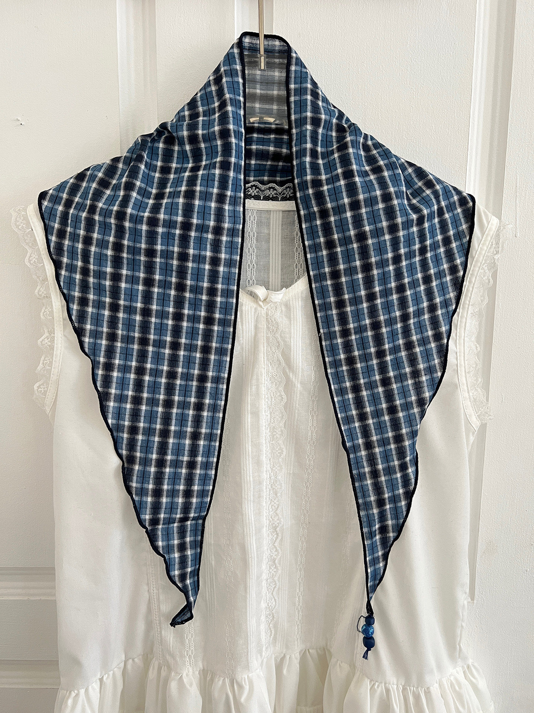 Blue and navy plaid triangle scarf draped open over a white garment