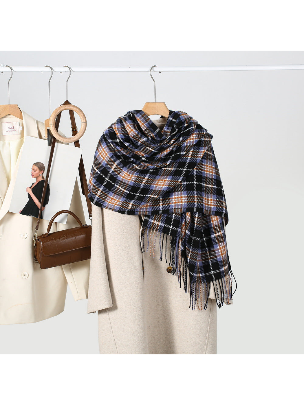 Black plaid scarf draped over a cream coat in a styled wardrobe scene